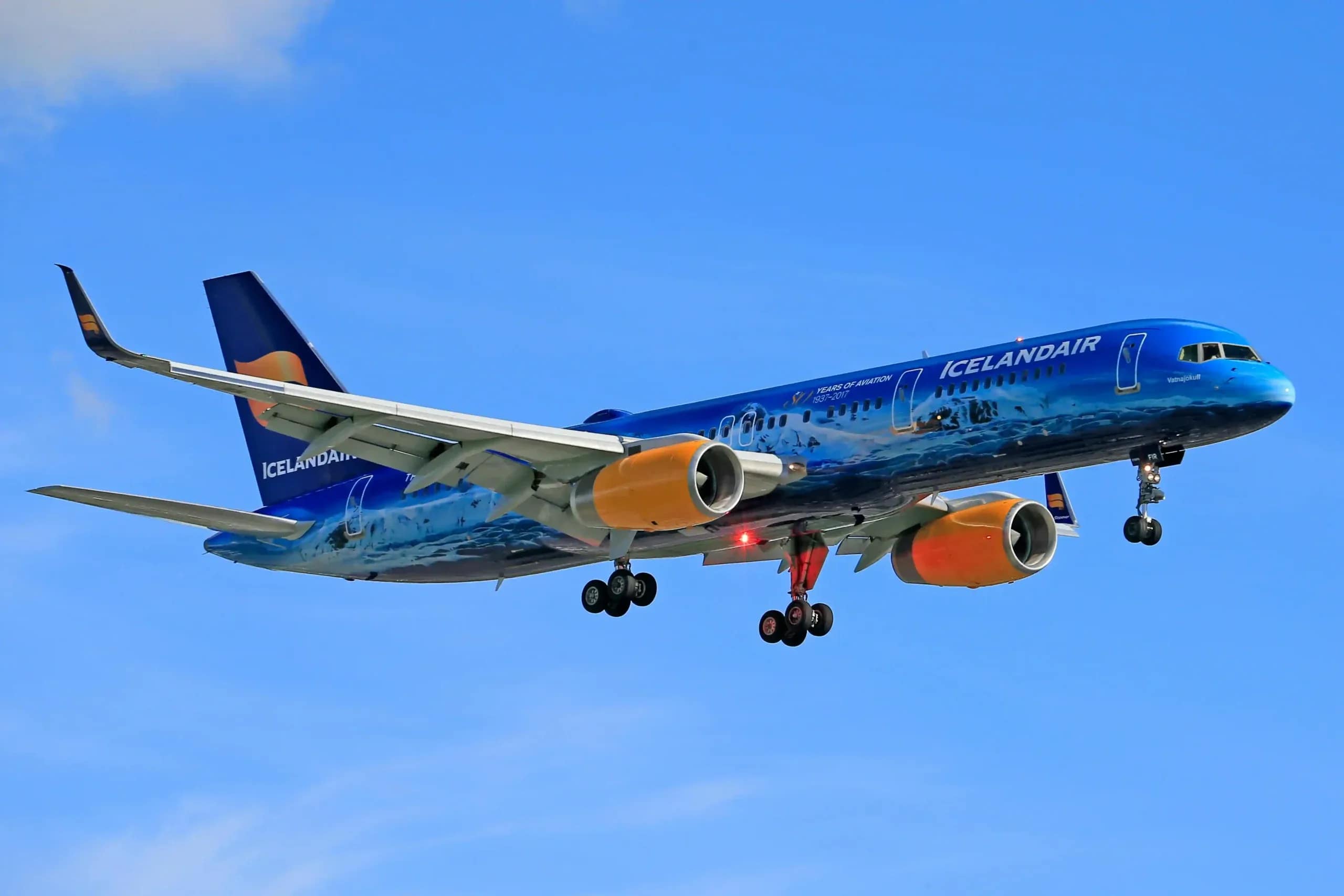 Blue Icelandair passenger jet descending for landing under a clear blue sky, representing travel to Iceland
