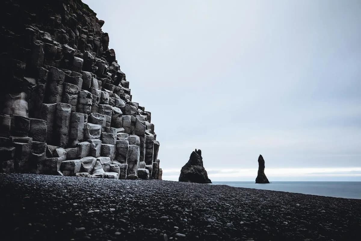 Basalt column cliffs and Reynisdrangar sea stacks at Reynisfjara Black Sand Beach, showing the rugged volcanic coastline of South Iceland.