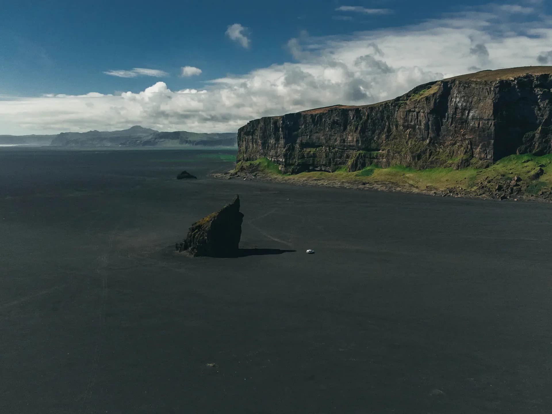 Campervan safety in Iceland shown on a black sand beach with steep cliffs and a vehicle driving in a remote coastal area