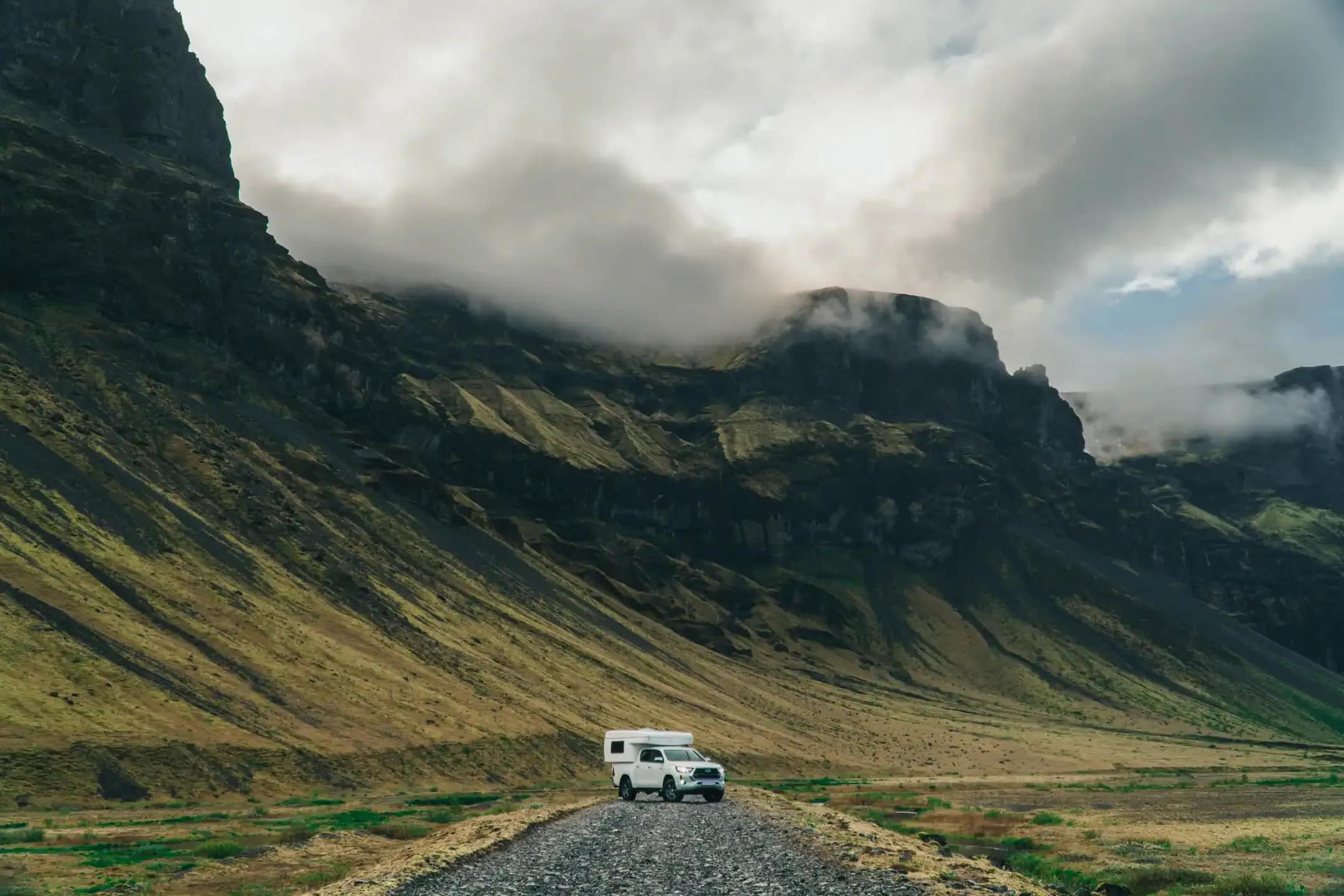 4x4 campervan driving through Iceland’s highland valley with steep green mountains and low-hanging clouds during a remote adventure