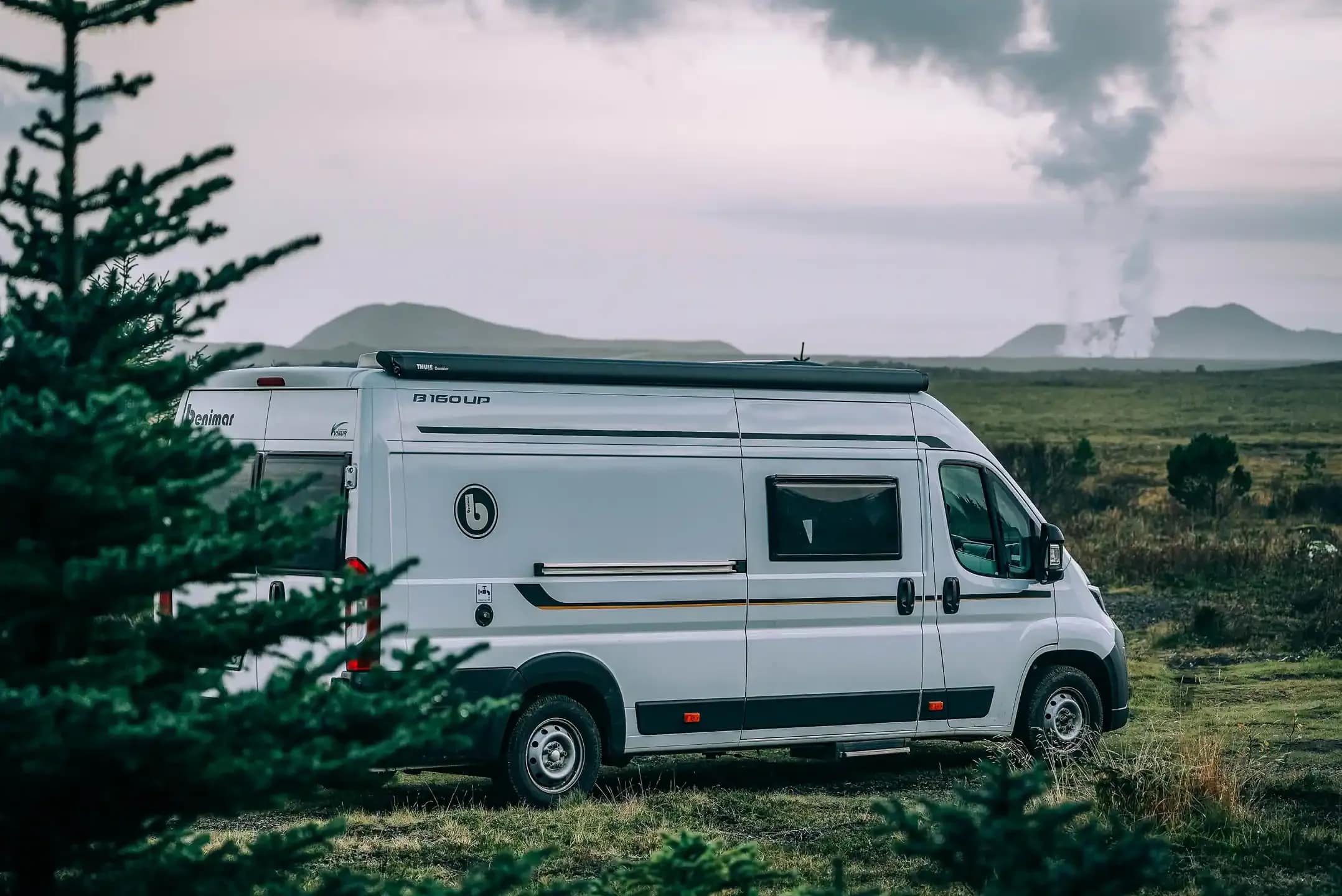 Campervan parked in Icelandic countryside with geothermal steam in the background during a scenic campervan road trip in Iceland