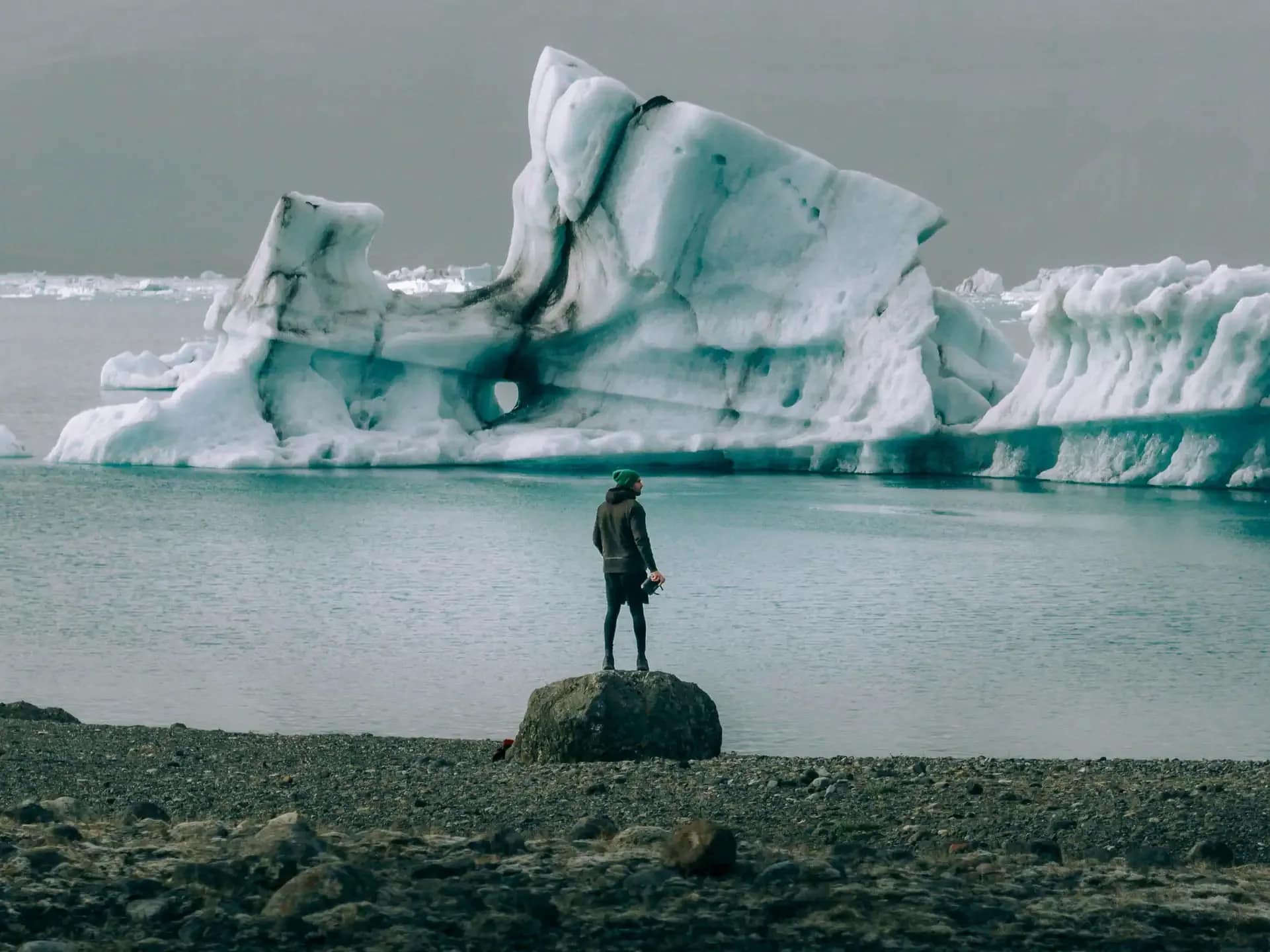 Traveler standing on rocky shore facing a floating iceberg in Vatnajökull National Park, Iceland