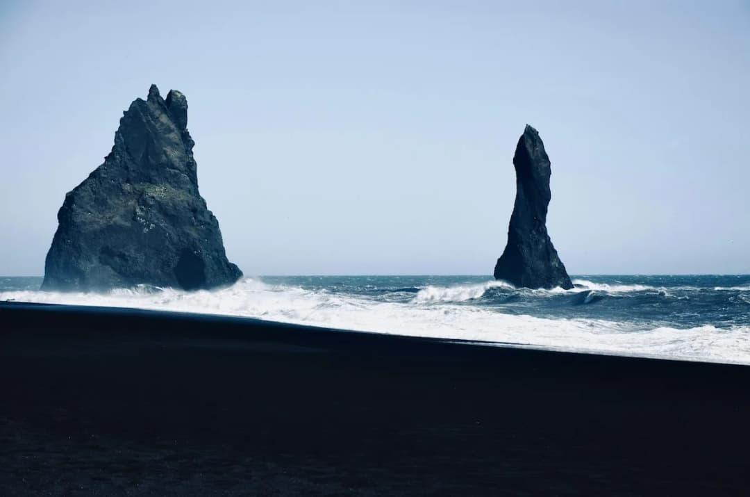 大西洋里的海蚀柱矗立在黑沙滩前，海浪拍打着南岸的火山海岸
