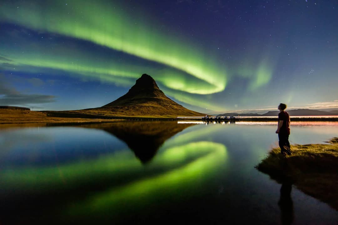 极光在冰岛草帽山（Kirkjufell）上空舞动，倒映在山前平静的湖面上