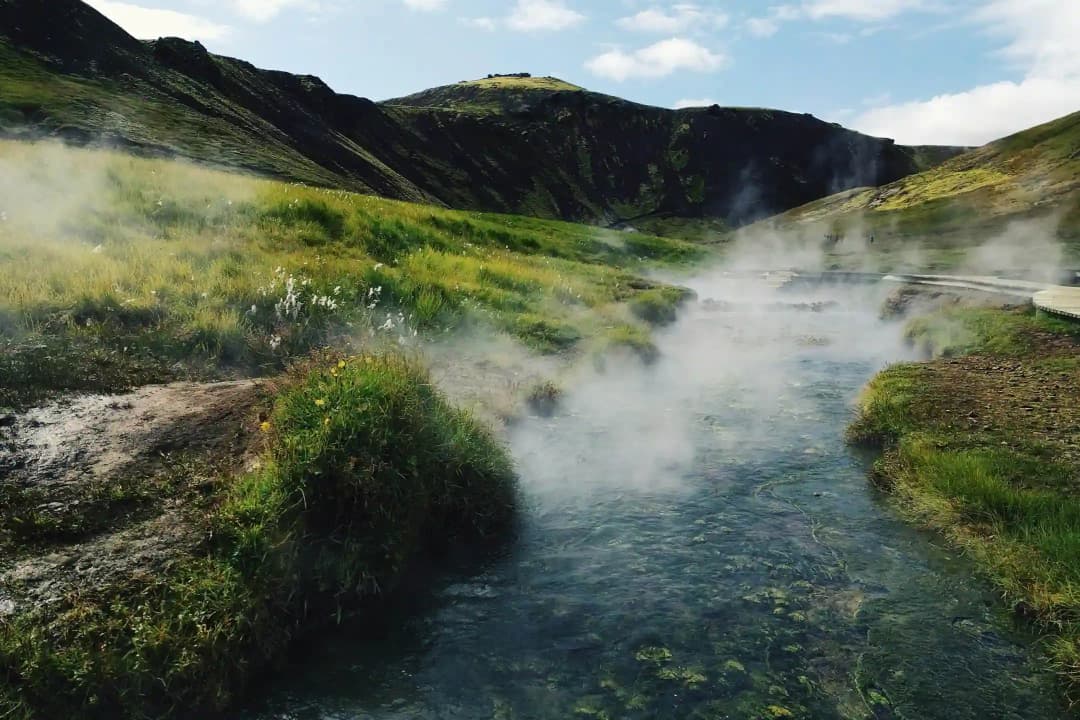 冰岛 Reykjadalur 温泉河，绿色山丘上方升起热气