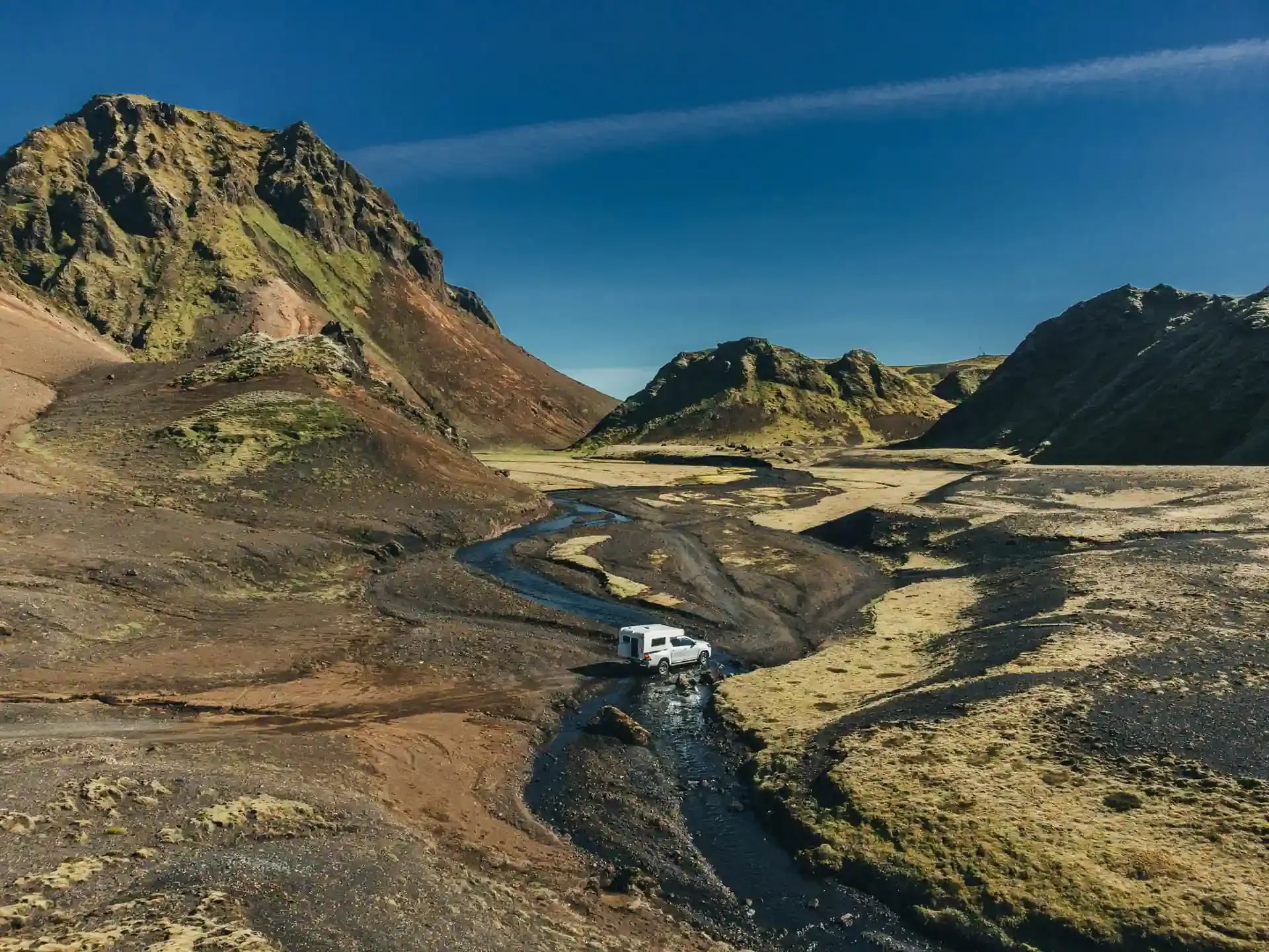 4x4 campervan rental in Iceland crossing a shallow river in the Highlands surrounded by colorful volcanic mountains on an F-road adventure