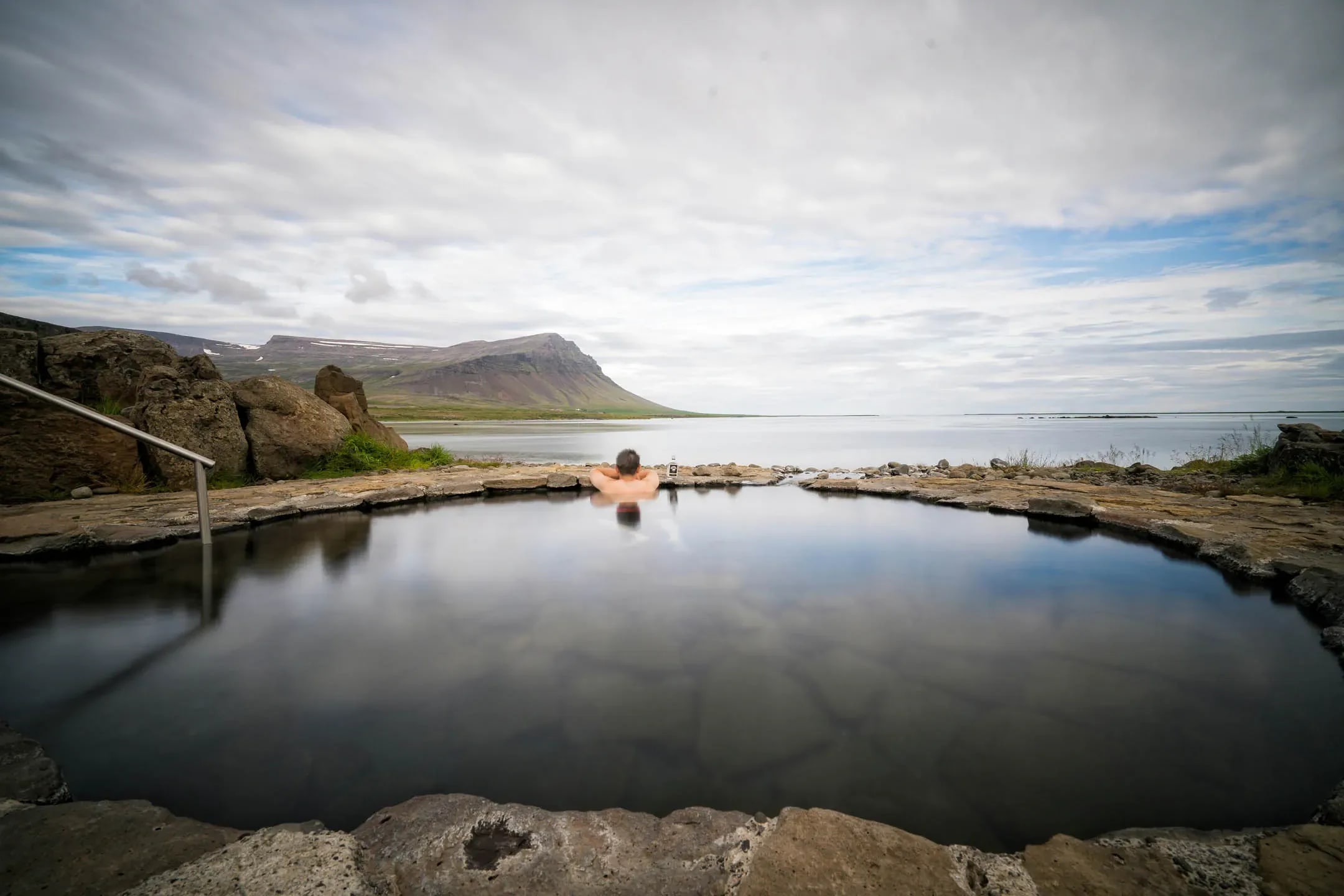 Outdoor geothermal swimming pool in Iceland with steam rising from warm water and mountains in the background