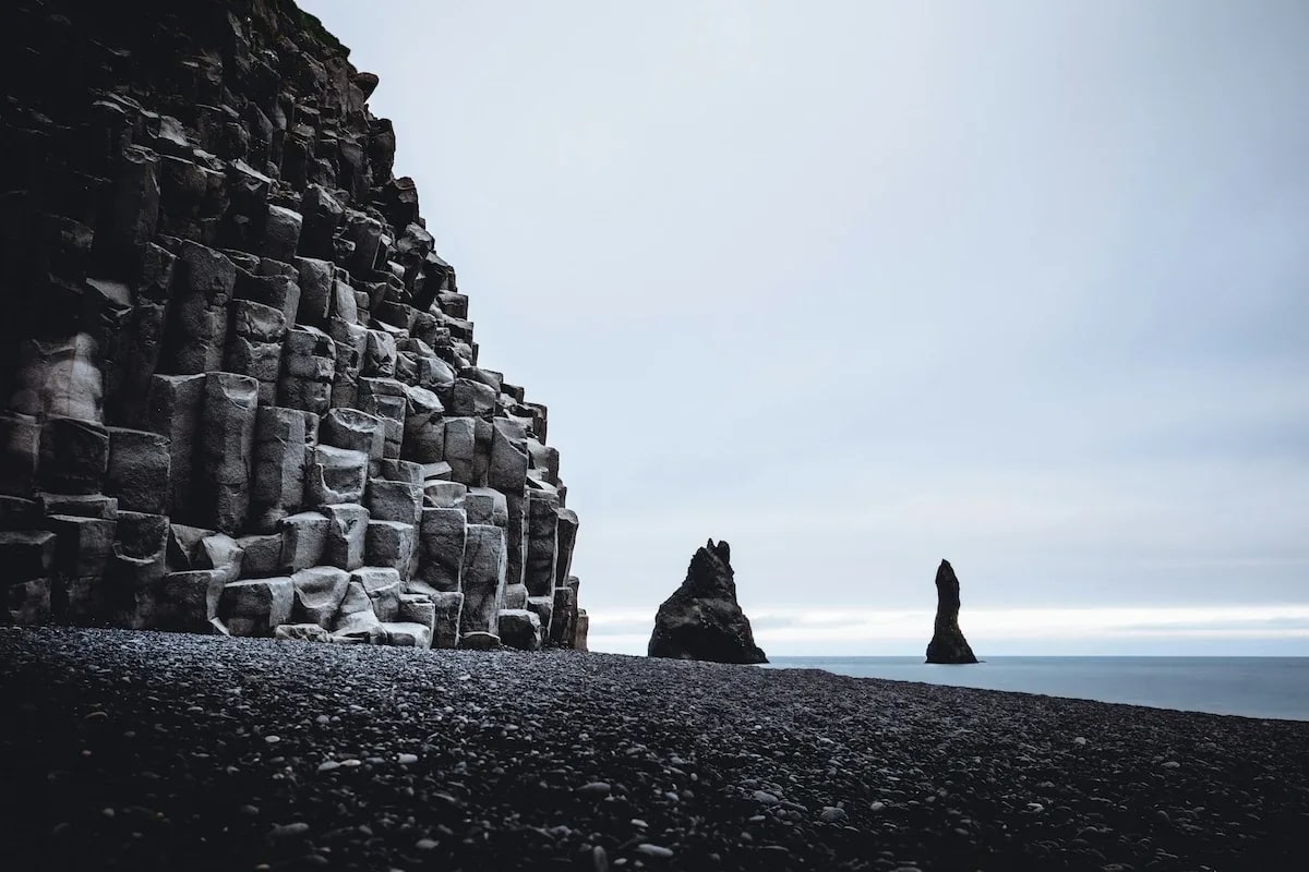 Basalt column cliffs and Reynisdrangar sea stacks at Reynisfjara Black Sand Beach, showing the rugged volcanic coastline of South Iceland.