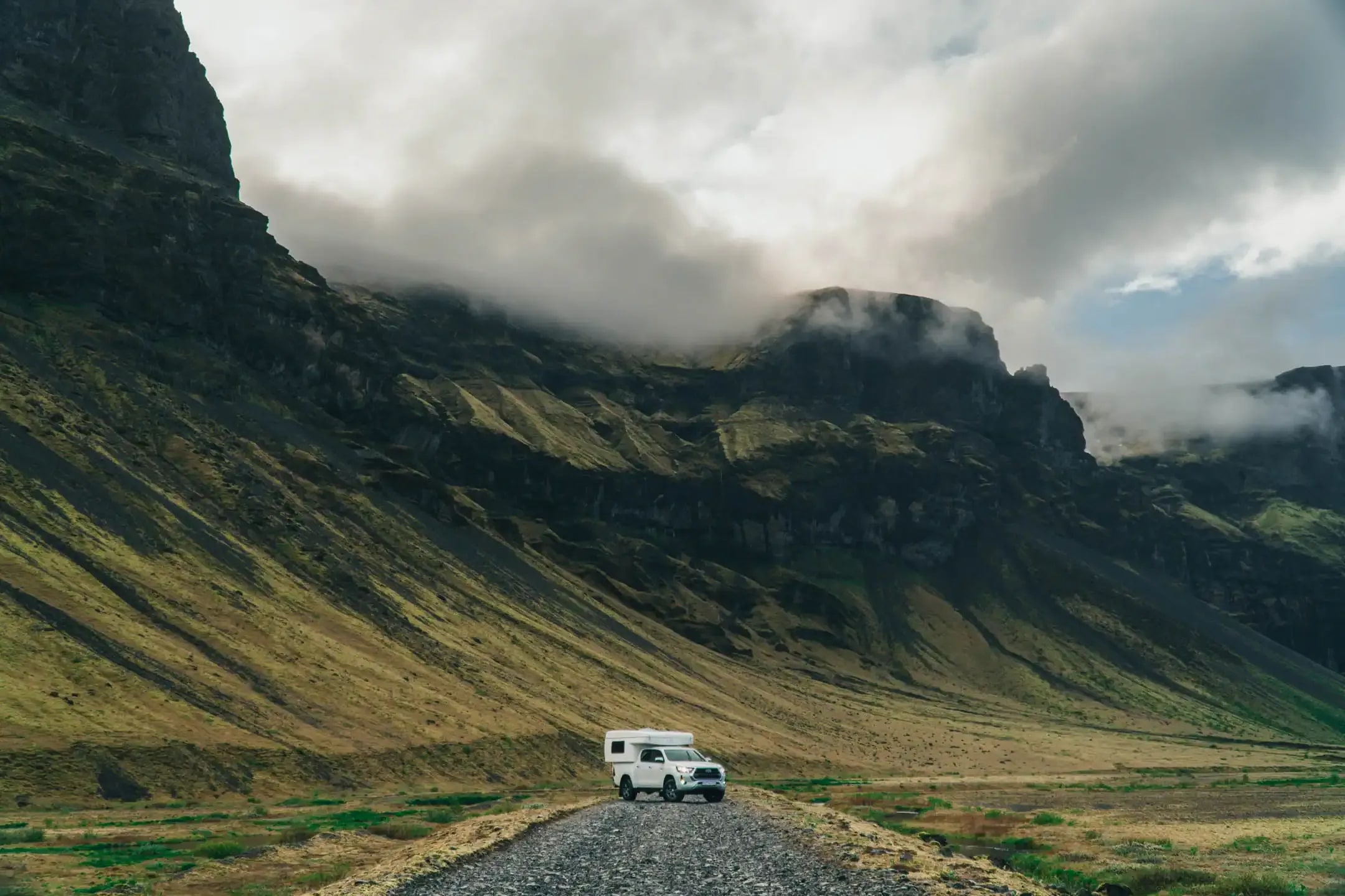 4x4 campervan driving through Iceland’s highland valley with steep green mountains and low-hanging clouds during a remote adventure