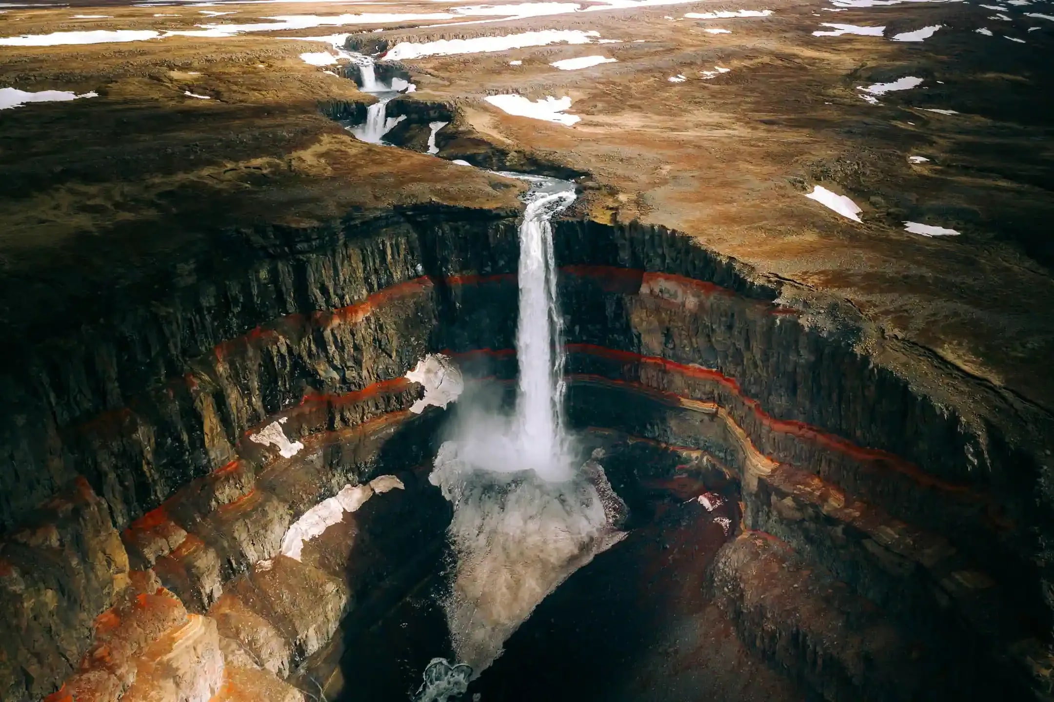 Drone view of Hengifoss waterfall in East Iceland cascading into a canyon marked by red volcanic strata